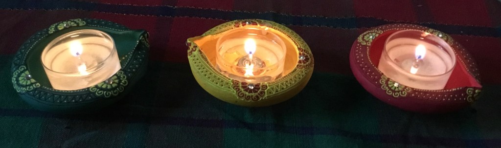 Three small circular incense holder, circular, bright red, green, and yellow, with lit tea candles inside. 