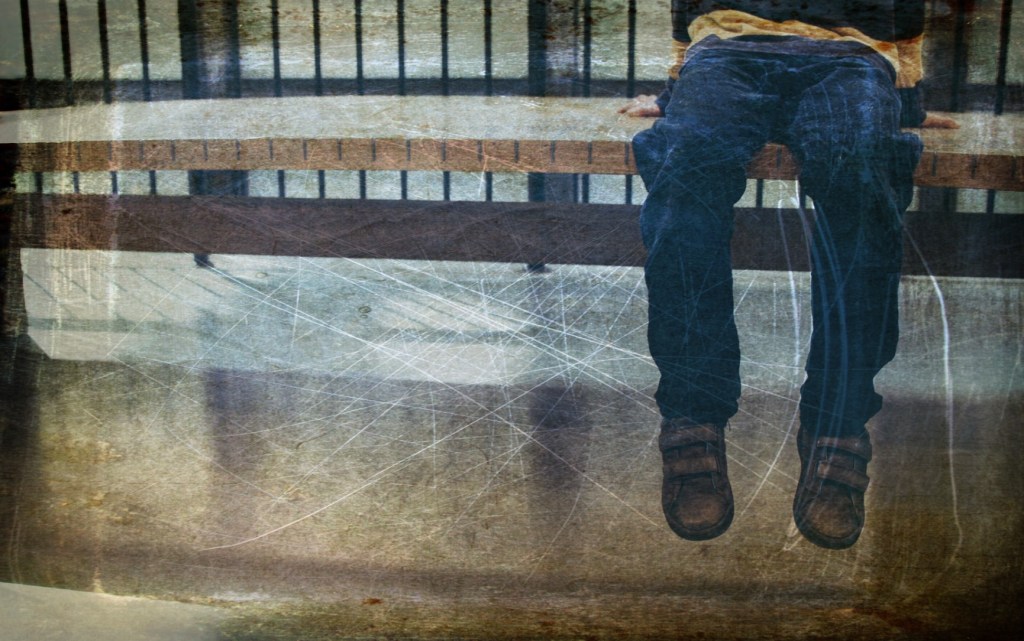 Young child sitting on high bench, with a railed banister behind. Only dangling legs, shoes, and a strip of bunched top are showing. The top appears to be striped yellow and brown, with long sleeves. The child wears jeans and brown leather shoes with Velcro straps. The original photograph is not distressed but I distressed it.   